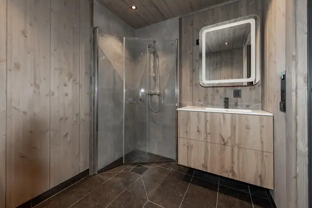 Badet er utstyrt med dusjhjørne, innfellbare dusjdører, veggmontert wc, servantskap, servant og mekanisk avtrekk.